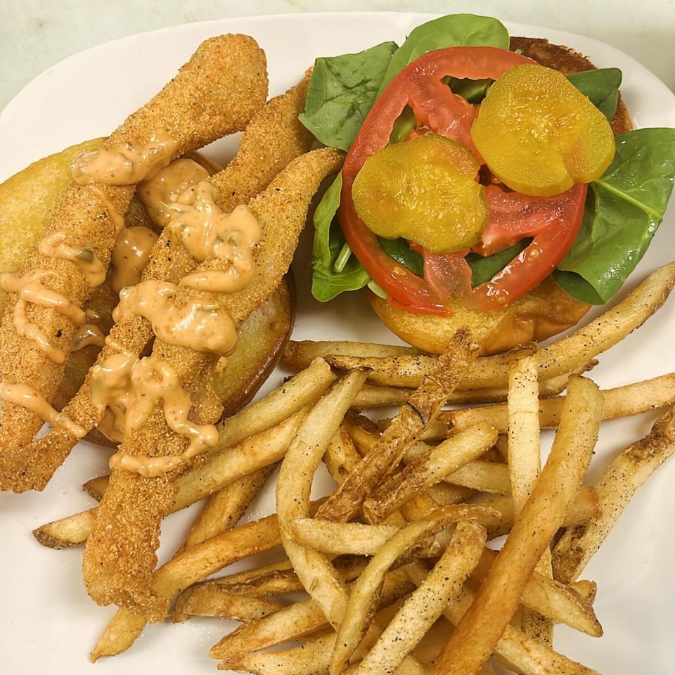Fried fish strips with sauce, a burger with tomato, spinach, and pickles, and french fries.