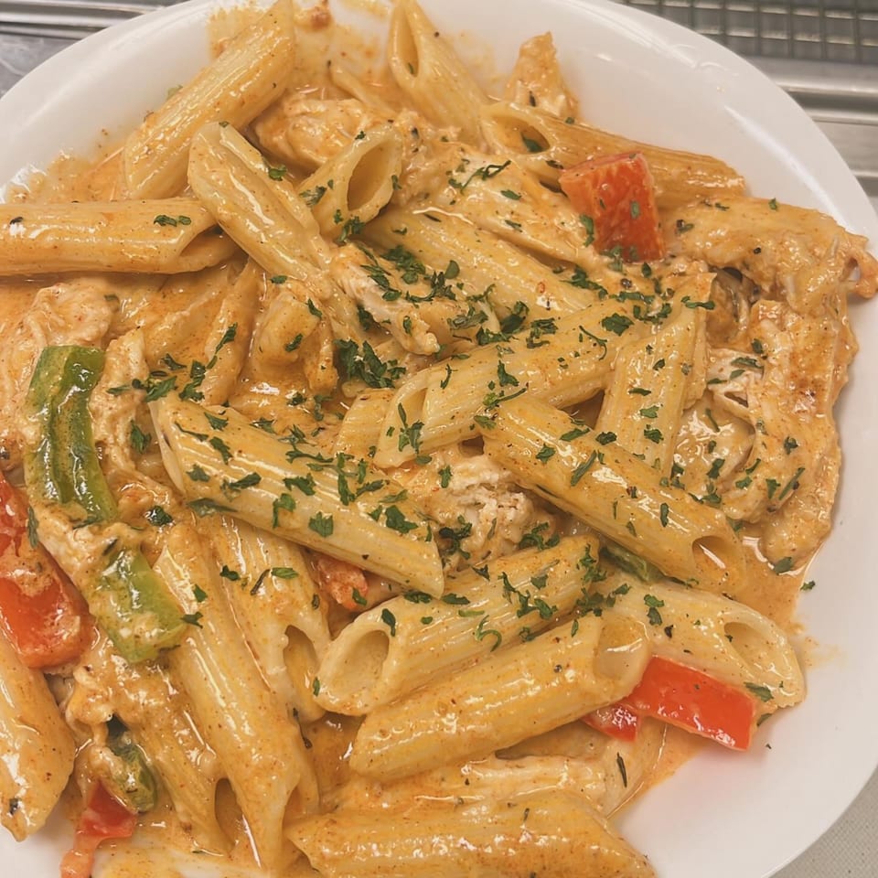 Penne pasta with creamy sauce, chicken, red and green bell peppers, and parsley.