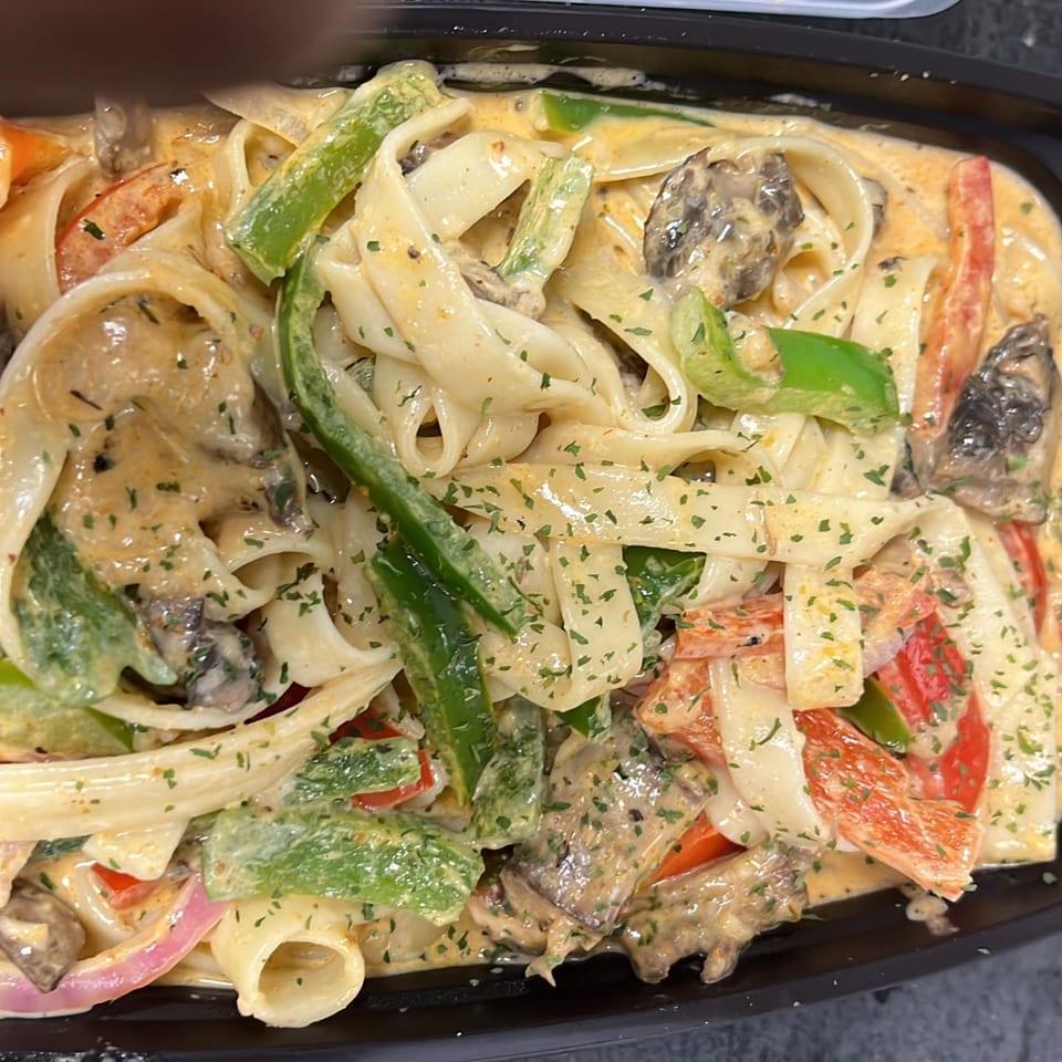 Creamy seafood pasta with bell peppers, onions, and mushrooms in a black container.